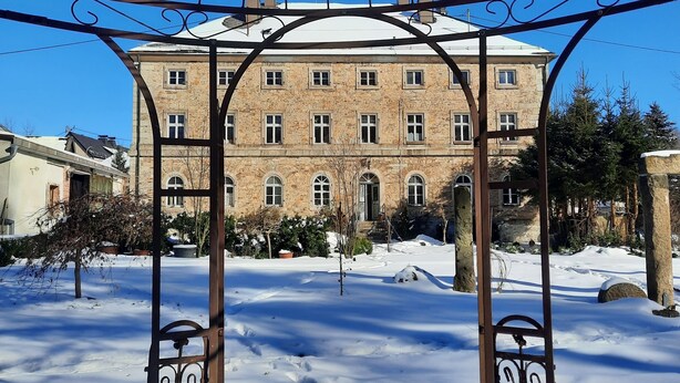 A gazebo with ornate metalwork, a stone building with multiple windows in the background, and a snow-covered ground. - Living in a stately home from 1848 in the Fichtelgebirge (Ebnath)