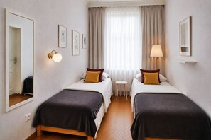 A hotel room with two beds, a small table, a mirror, and a window with curtains.