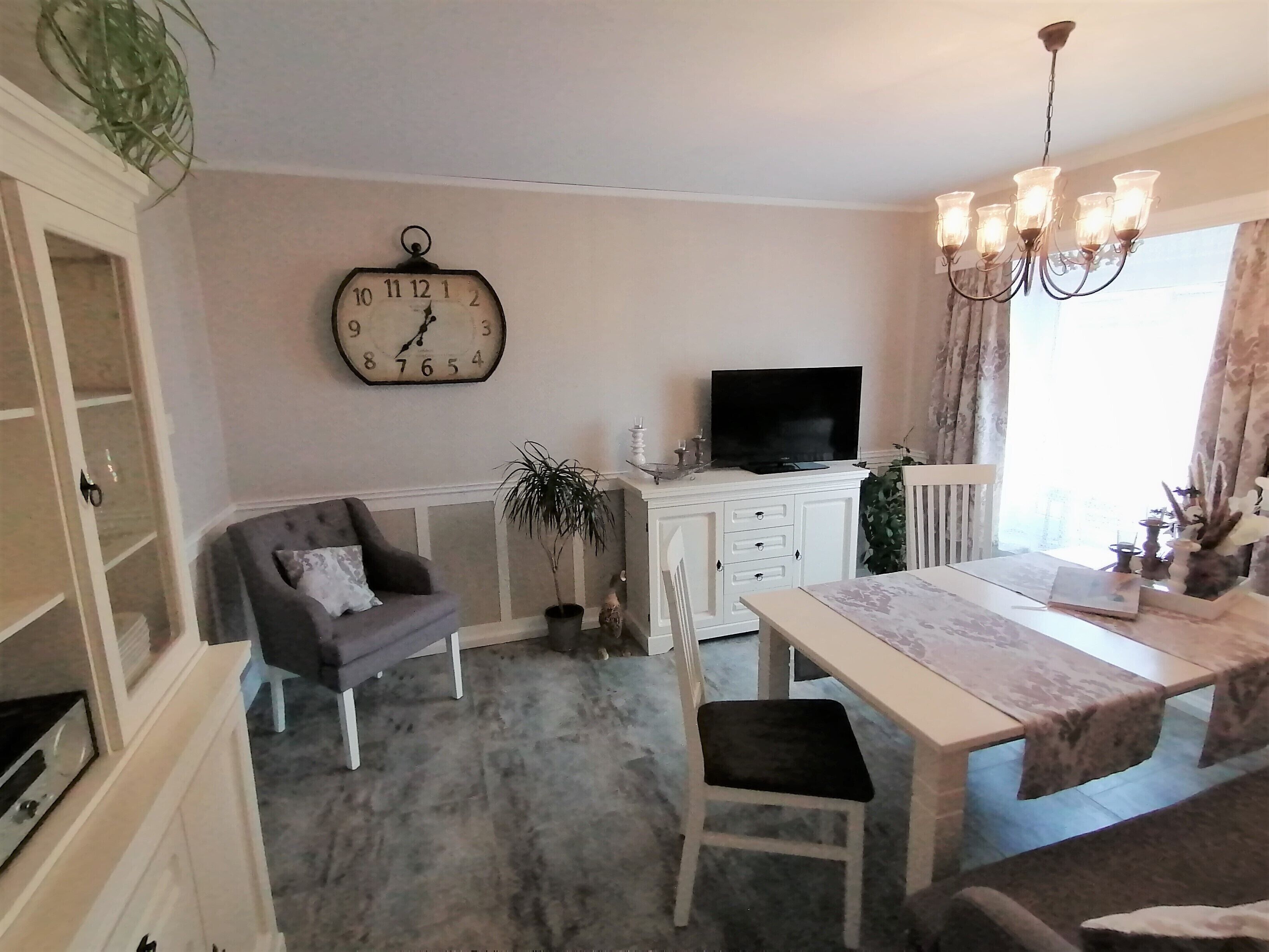 Una sala de estar con un sofá, una mesa de comedor, un televisor y un reloj en la pared.