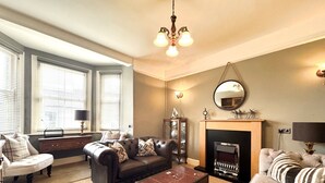 A living room with a fireplace, leather sofas, a wooden coffee table, and a large window with blinds. - Short summer breaks available!! (St Davids)