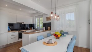 A modern kitchen with white cabinets, a black stove, and a wooden countertop. There is a dining table with blue chairs and a fruit bowl. - Nice home in Bregi with sauna (Bregi)