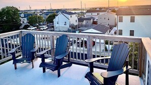 A deck with three Adirondack chairs overlooking a residential area during sunset. - The Lighthouse- Gameroom, RooftopDeck! Beach badges,chairs,cart incld (Seaside Heights)