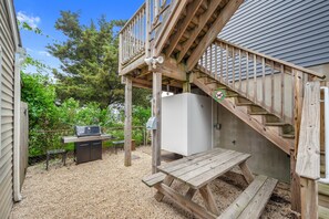 A wooden deck with a grill and picnic table, surrounded by a gravel area and greenery. - The Lighthouse- Gameroom, RooftopDeck! Beach badges,chairs,cart incld (Seaside Heights)