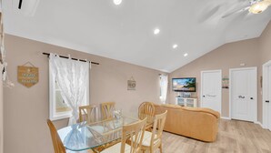 A dining area with a glass table and wooden chairs, a beige sofa, and a television in the background. - The Lighthouse- Gameroom, RooftopDeck! Beach badges,chairs,cart incld (Seaside Heights)
