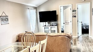 A living room with a sofa, a TV, a dining table with chairs, and a wooden floor. - The Lighthouse- Gameroom, RooftopDeck! Beach badges,chairs,cart incld (Seaside Heights)