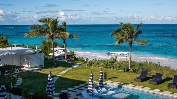 A pool area with lounge chairs and umbrellas, a beach with palm trees, and a view of the ocean.