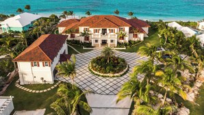 A large, two-story house with a tiled roof, surrounded by palm trees and a view of the ocean.