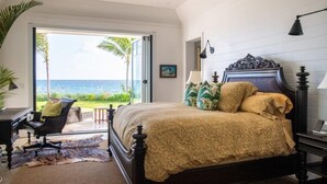 A bedroom with a large bed, a desk, and a chair. There is a view of the ocean through a glass door.