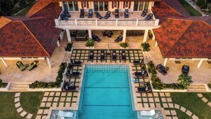 An aerial view of a large house with a swimming pool, multiple lounge areas, and a covered patio.