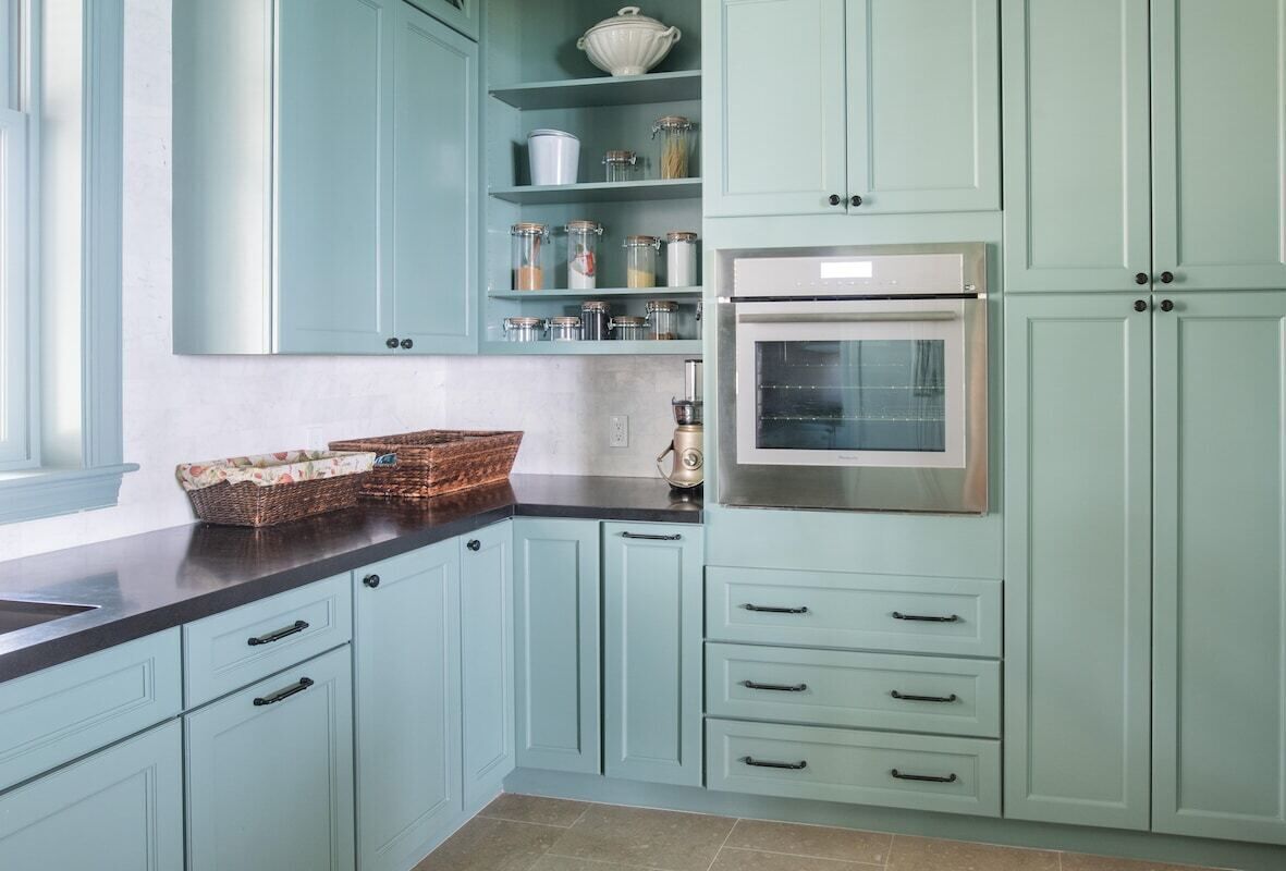 A kitchen with light blue cabinets, a stainless steel oven, and a countertop with a basket.