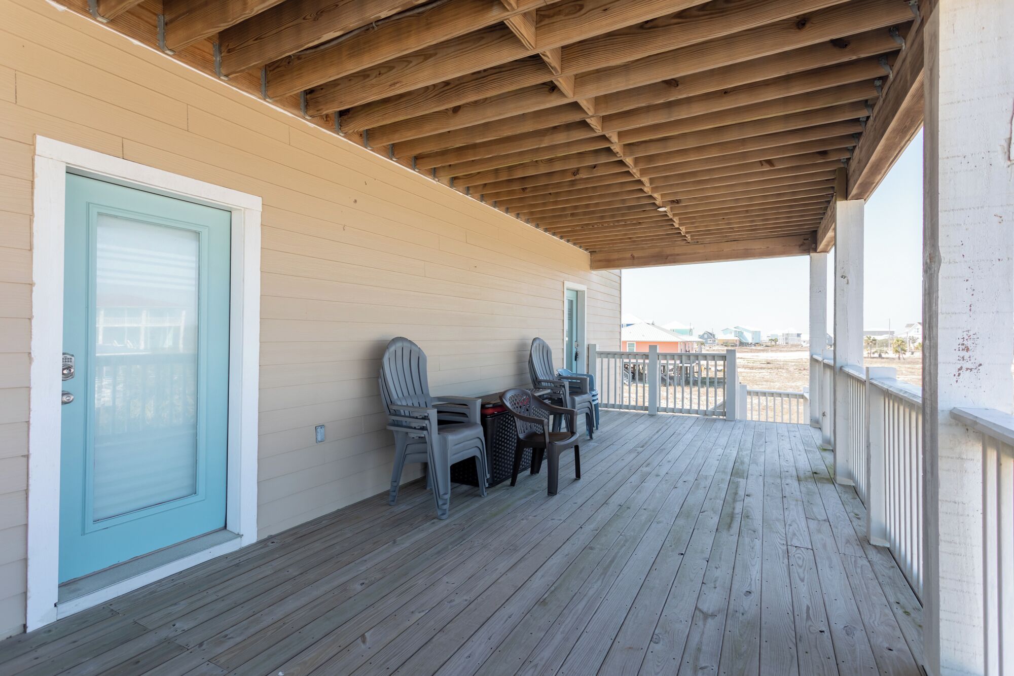 A covered porch with a wooden ceiling, a light blue door, and a view of the beach.