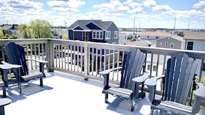 Een balkon met vier Adirondack-stoelen en een kleine tafel, met uitzicht op een woonwijk met huizen en een heldere lucht.