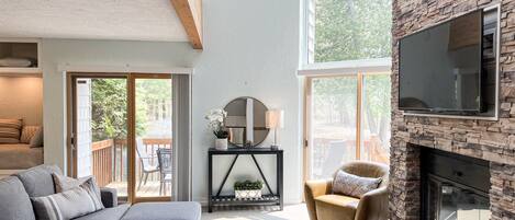 A modern living room with a stone fireplace, a large TV mounted on the wall, and a cozy seating area with a sofa and armchairs.