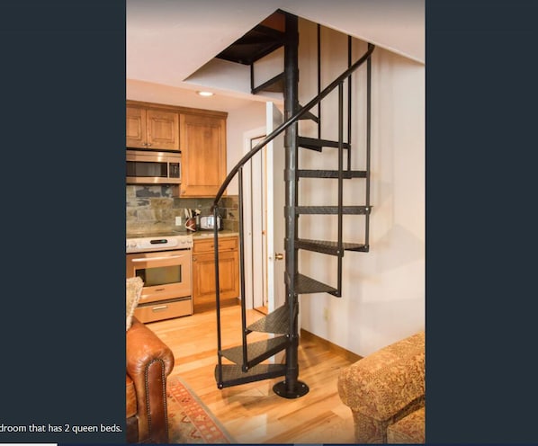 Compact living space with a modern kitchen, spiral staircase, and two queen beds.