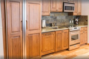 Kitchen features a stainless steel sink, double oven, and microwave, along with a dish rack and wooden cabinetry.