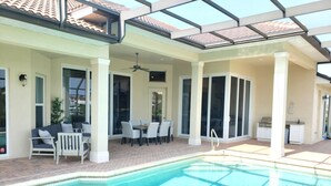 A swimming pool with a tiled deck, a covered patio area with outdoor furniture, and a kitchen area with a grill. - Marco Island Waterfront Home w/Heated Pool, Bikes, < 2 Miles to the Beach (Marco Island)