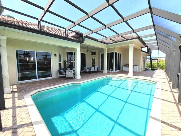 A covered swimming pool with a patio area, sliding glass doors, and a ceiling fan. - Marco Island Waterfront Home w/Heated Pool, Bikes, < 2 Miles to the Beach (Marco Island)