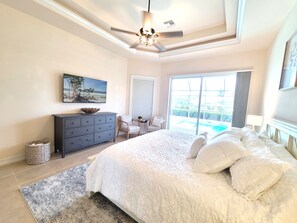 A bedroom with a large bed, a dresser, a chair, a small table, and a view of a swimming pool through a sliding door. - Marco Island Waterfront Home w/Heated Pool, Bikes, < 2 Miles to the Beach (Marco Island)