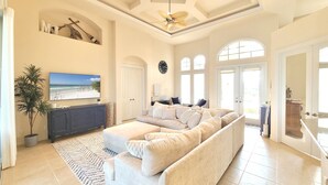 A spacious living room with a large beige sectional sofa, a flat-screen TV mounted on the wall, and a ceiling fan. - Marco Island Waterfront Home w/Heated Pool, Bikes, < 2 Miles to the Beach (Marco Island)