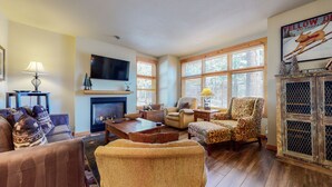 Un salon chaleureux avec une cheminée, des fauteuils confortables, un téléviseur et de grandes fenêtres.