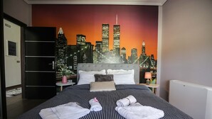Quarto de hotel com cama, mesa de cabeceira, luminária e um mural com vista urbana na parede.