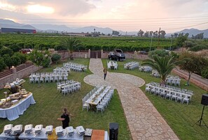 An outdoor event with tables set up for dining, a stage, and a scenic backdrop of mountains and greenery.