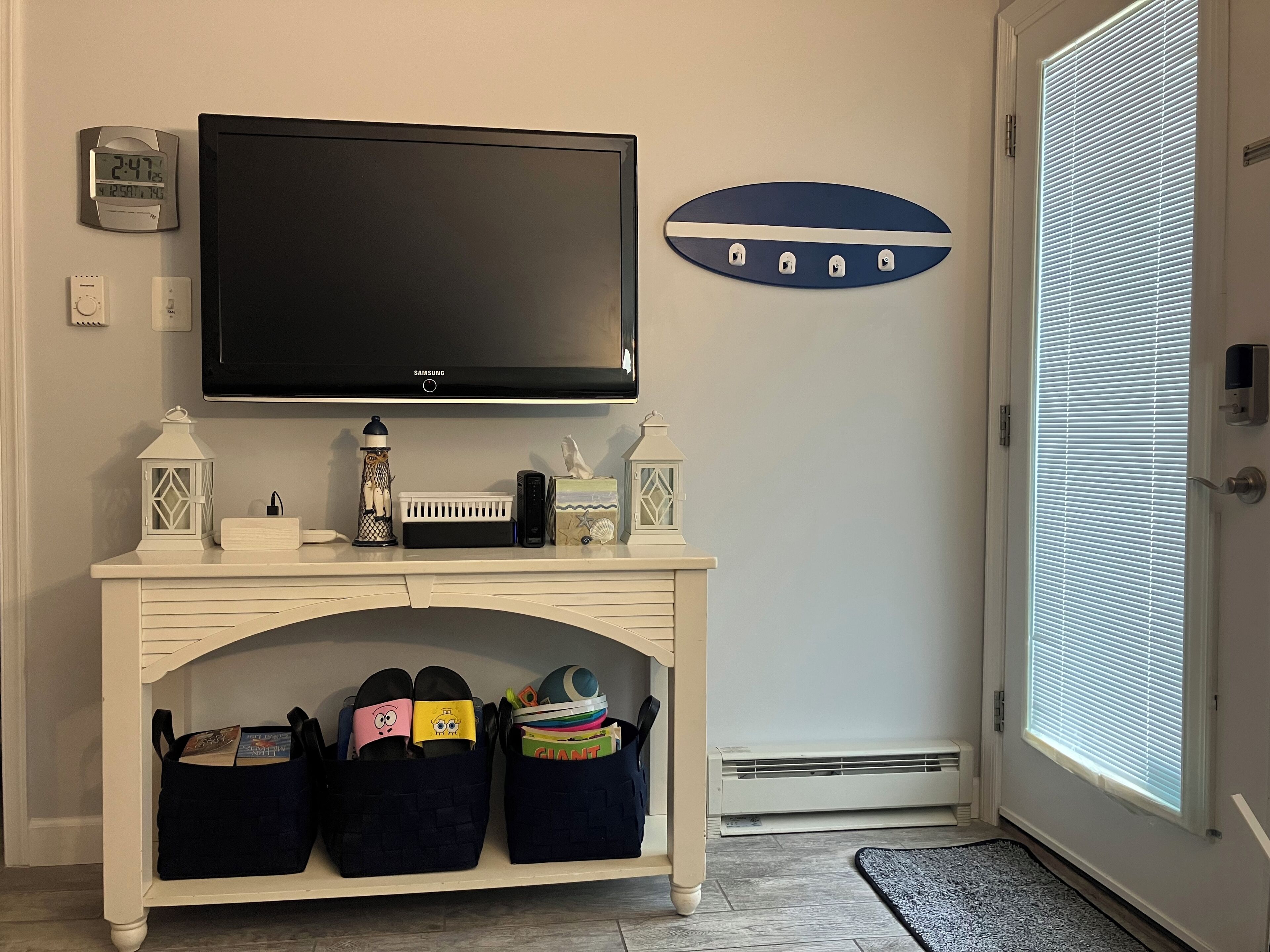 A living room with a flat-screen TV, a white fireplace, storage bins, and a decorative wall piece.