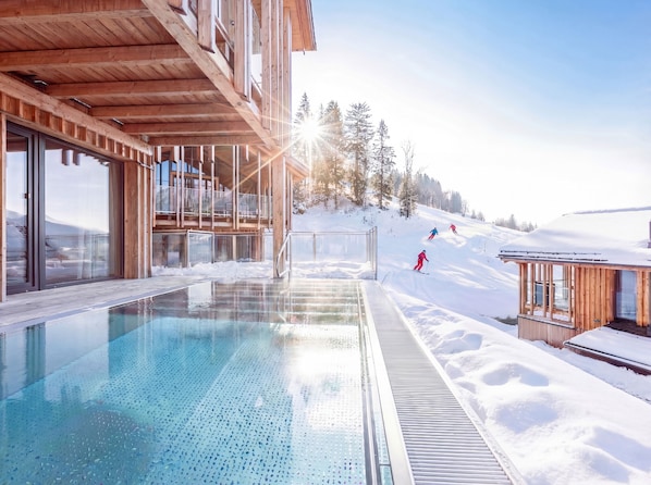 A wooden building with a pool, ski slope, and snowy landscape.