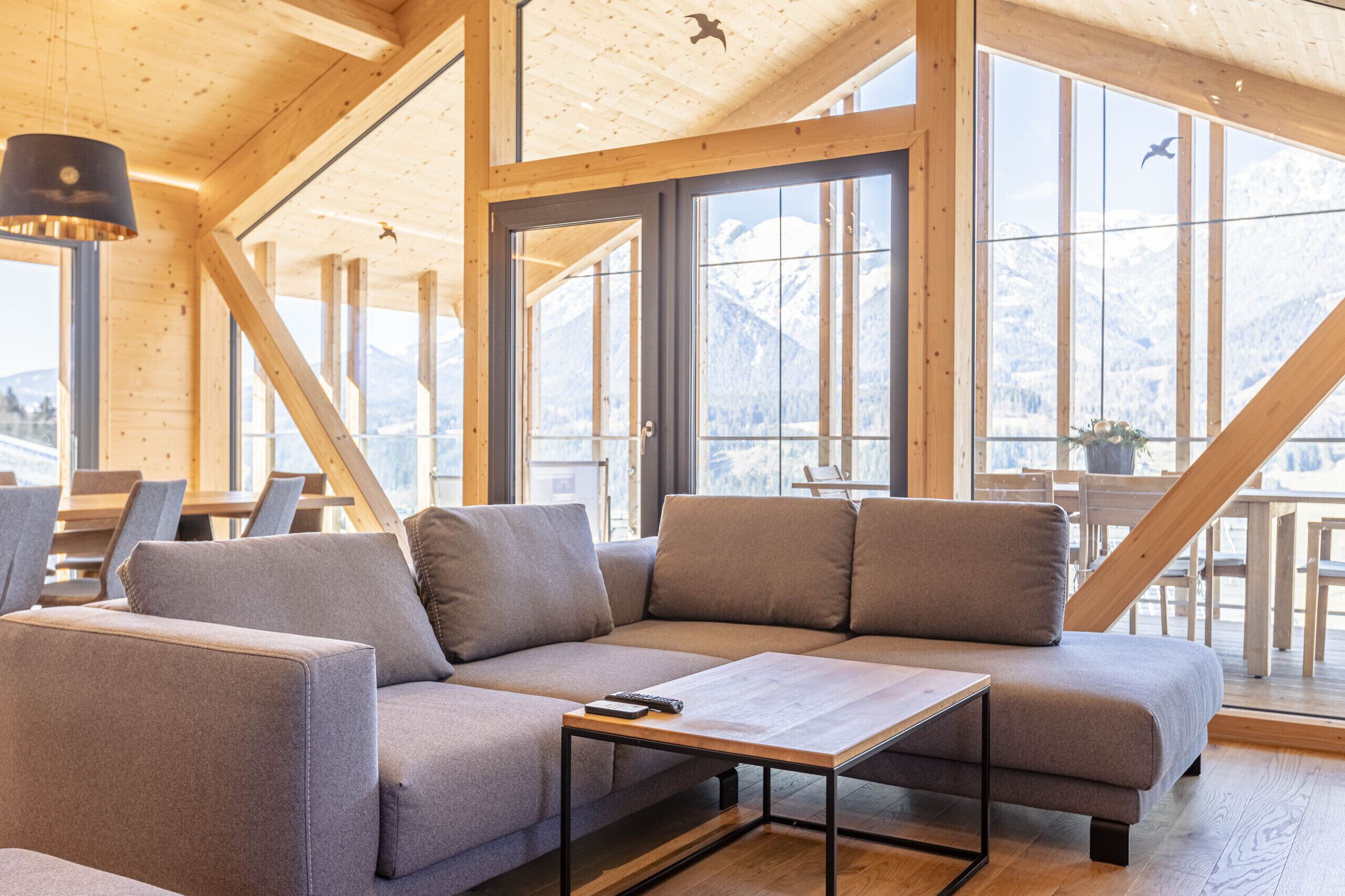 Ein modernes Interieur mit einer Eckcouch, einem kleinen Tisch und großen Fenstern mit Blick auf die Berge.