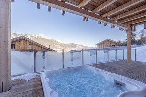 Une terrasse en bois avec un jacuzzi donnant sur un paysage enneigé et des montagnes.