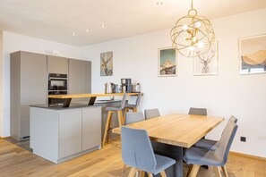 Une cuisine moderne avec des meubles gris, une table à manger en bois et des chaises bleues. Un lustre est suspendu au-dessus de la table.