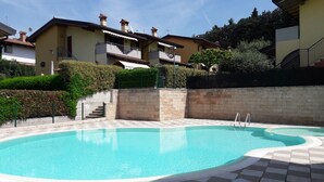Une piscine dotée d’une terrasse carrelée, entourée d’un mur de pierre et d’une haie.