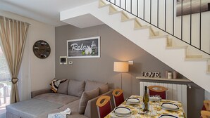 Un salon chaleureux avec un canapé, une table à manger dressée pour deux personnes, un escalier et un panneau indiquant « Détendez-vous » sur le mur.