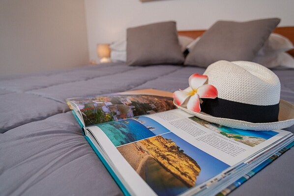 A bed with a magazine, a hat, and a flower.