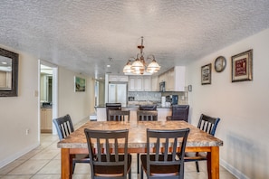 A spacious kitchen with a central island, white cabinets, and a dining area with a marble table and chairs. - Sand Dollar 107 Gorgeous Beachfront Views, Spacious, Pool, BBQ, Private Pier (Indian Shores)