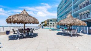 Een dak terras met rieten parasols, een zwembad en uitzicht op een blauw gebouw.
