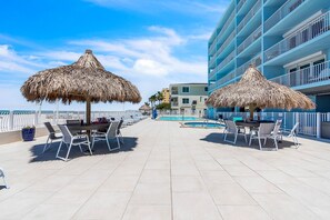 A rooftop terrace with thatched umbrellas, a pool, and a view of a blue building.