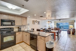 A modern kitchen with a central island, built-in appliances, and a dining area with a view. - Sand Dollar 107 Gorgeous Beachfront Views, Spacious, Pool, BBQ, Private Pier (Indian Shores)