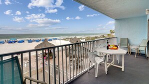Een balkon met uitzicht op het strand, een tafel met een fles en fruit, en een stoel.