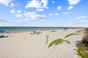 A beach with clear skies, people sunbathing, and beach umbrellas.
