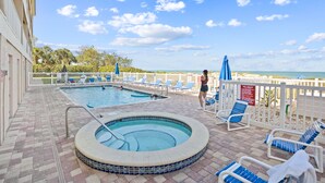 A pool area with a hot tub, lounge chairs, and a view of the beach. - Oceanside302 Beachfront- Gorgeous Gulf Views, lots of updates, great location (Indian Rocks Beach)