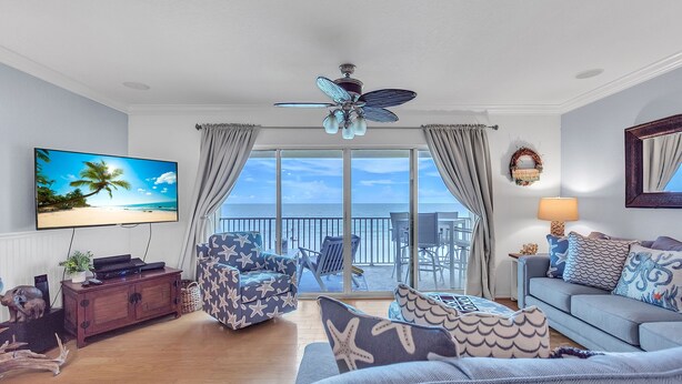 A living room with a TV, ceiling fan, and a view of the ocean. - Oceanside302 Beachfront- Gorgeous Gulf Views, lots of updates, great location (Indian Rocks Beach)