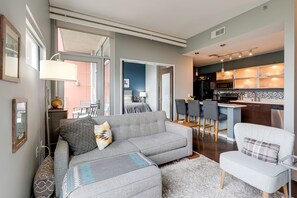 A modern living room with a grey sofa, a white armchair, and a kitchen area with a bar and dining space. - Smart, Stylish Music City Condo - Concierge, Restaurants, Gym, Rooftop Patio, Parking (Nashville)