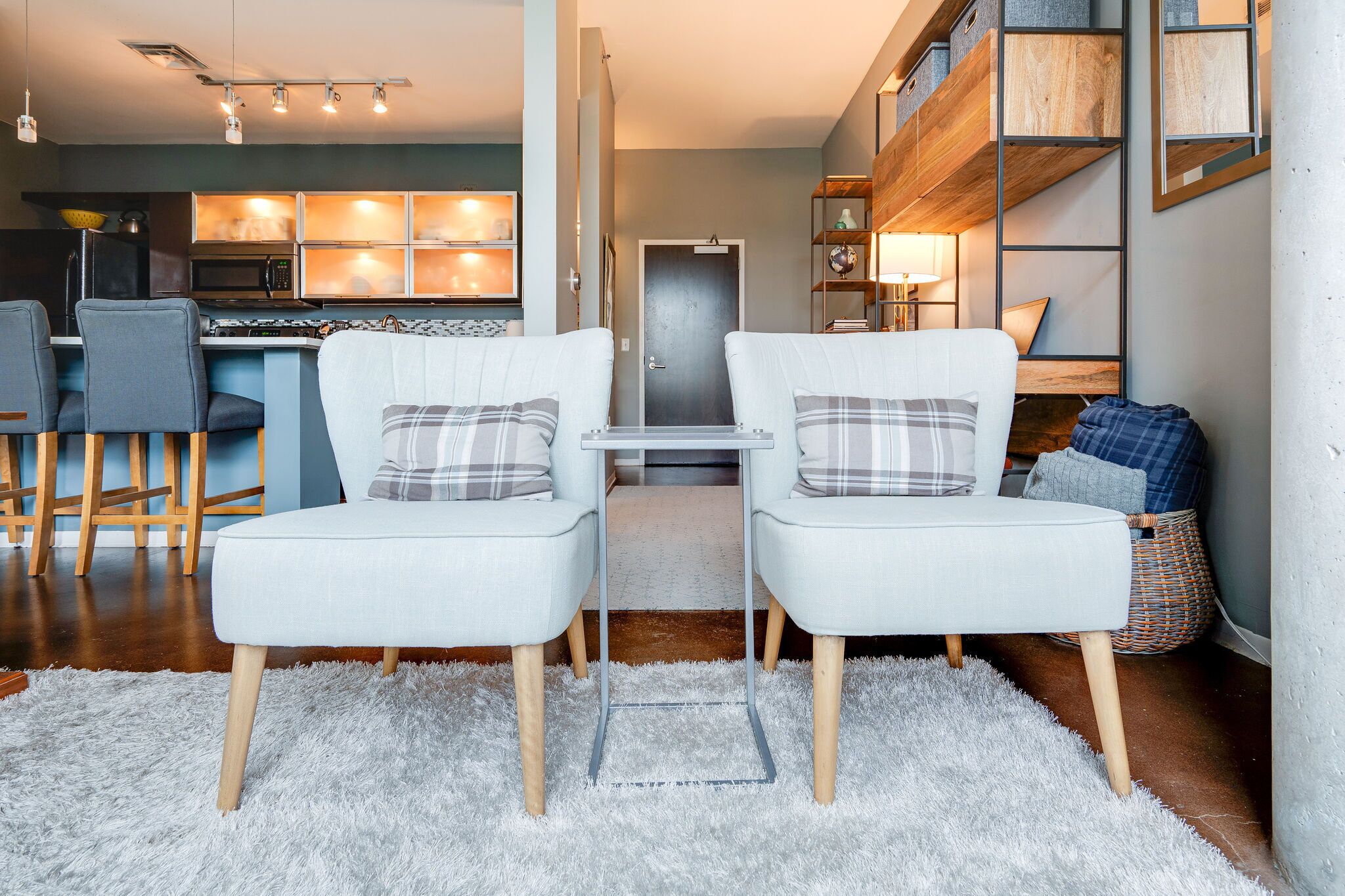 A modern living room with two white armchairs, a small table, and a kitchen in the background.