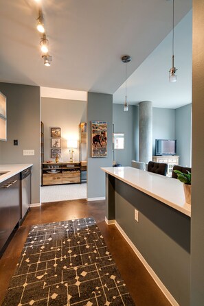 A modern kitchen with a central island, a dining area with a bar, and a living space with a TV and seating. - Smart, Stylish Music City Condo - Concierge, Restaurants, Gym, Rooftop Patio, Parking (Nashville)