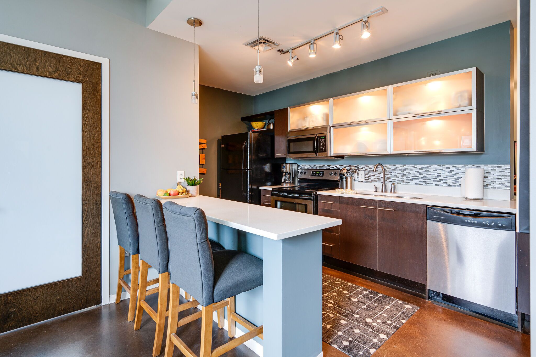 A modern kitchen with a central island, dark cabinetry, stainless steel appliances, and a tiled backsplash.