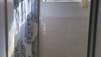 Une petite salle de bain avec des toilettes, un rideau de douche orné d’un motif cachemire, une fenêtre donnant sur des arbres et un rouleau de papier toilette accroché au mur.