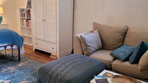 Ett mysigt vardagsrum med en beige soffa, en mönstrad matta, ett vitt skåp och en bokhylla.