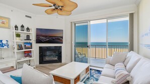 Amplia sala de estar con televisor grande, chimenea y balcón con vistas a la playa.