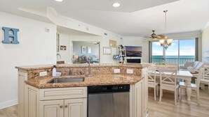 Una cocina moderna con encimeras de granito, lavavajillas y un comedor con vista al océano.